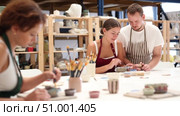 Experienced potter helps students learn how to make patterns on ceramic plates using paint and brush in a pottery workshop. Стоковое видео, видеограф Яков Филимонов / Фотобанк Лори