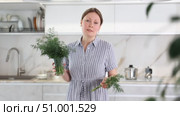 Woman in dress with short sleeves sitting near kitchen table and holding glass with bunch of dill. Стоковое видео, видеограф Яков Филимонов / Фотобанк Лори