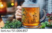 A person enjoys a warm cup of herbal tea made with fresh ingredients, surrounded by greenery and a warm, inviting setting. Стоковое AI-видео, аниматор Данила Большаков / Фотобанк Лори