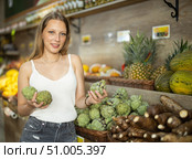 Girl client near vegetable stand in store choose artichoke. Стоковое фото, фотограф Яков Филимонов / Фотобанк Лори