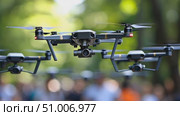 Drones hover above a busy park filled with people, showcasing their aerial capabilities against a backdrop of trees and bright skies. Стоковое AI-видео, аниматор Данила Большаков / Фотобанк Лори