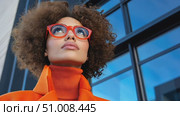 A stylish woman in a bold orange ensemble stands confidently, highlighting her chic look against a bright blue sky over the city. Стоковое AI-видео, аниматор Данила Большаков / Фотобанк Лори