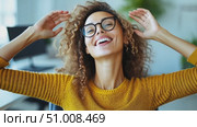 A cheerful young woman with curly hair and glasses enjoys a moment of relaxation in her stylish office, radiating positivity and confidence. Стоковое AI-видео, аниматор Данила Большаков / Фотобанк Лори