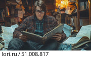 A young scholar sits cross-legged, deeply engaged with an ancient book, surrounded by scattered manuscripts and notes in a dimly lit library. Стоковое AI-видео, аниматор Данила Большаков / Фотобанк Лори