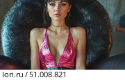 A fashion model exudes confidence in a shiny pink outfit, sitting elegantly in a distinctive black chair against an artistic backdrop. Стоковое AI-видео, аниматор Данила Большаков / Фотобанк Лори