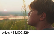 Teenager is thoughtfully watching the sunrise, immersed in his thoughts as he relaxes in nature. Close up. Стоковое видео, видеограф Strunov David / Фотобанк Лори