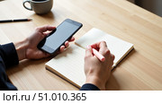 Человек держит смартфон и записывает информацию в блокнот. / A person holds a smartphone and writes information in a notebook. Стоковое AI-изображение, AI-художник Валерий Лукин / Фотобанк Лори