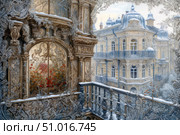 A magnificent image of a fairy-tale architectural ensemble in winter. A richly decorated facade with carved patterns and ornate ornaments in the Baroque or Art Nouveau style. The snowy layer gives the picture an atmosphere of magic and silence. Blooming plants can be seen through the finely carved window, contrasting with the cold outside. The view from the balcony opens up a perspective of a majestic building with domes and wrought-iron balconies. Ideal for themes of architecture, winter fairy tales, fantasy, decorative art. Стоковое AI-изображение, AI-художник Анна Кривицкая / Фотобанк Лори
