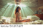 A young woman sits on her bed, mesmerized by the enchanting light and water reflections enveloping her room at dawn. Стоковое AI-видео, аниматор Данила Большаков / Фотобанк Лори