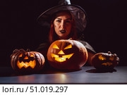 An ominous witch in a hat conjures over a jack-o-lantern. Traditional halloween characters. Mystical fog creeps over pumpkins with carved terrible faces. An evil witch casts a spell. Стоковое фото, фотограф Михаил Решетников / Фотобанк Лори