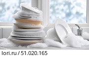 Dishes accumulate suds in a bright kitchen during winter cleanup. Стоковое AI-изображение, AI-художник Katsiaryna Repich / Фотобанк Лори