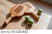 Two wooden pickleball paddles with green balls on wooden floor. Стоковое AI-изображение, AI-художник Катерина Бондарец / Фотобанк Лори