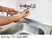 Removal of long spout from kitchen sink shows hands detaching straight spout from sink faucet body with water control valves visible near faucet. Стоковое фото, фотограф Владимир Григорьев / Фотобанк Лори