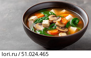 Delicious versa miso soup with tofu, mushrooms, spinach, and carrot served warm. Стоковое AI-изображение, AI-художник Katsiaryna Repich / Фотобанк Лори