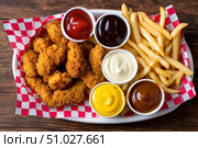 Breaded chicken strips and french fries with various sauces on wooden table. Стоковое AI-изображение, AI-художник Юрий Поздников / Фотобанк Лори