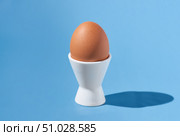 One brown chicken egg stands in a white egg-cup on a blue background. Стоковое фото, фотограф Екатерина Лызлова / Фотобанк Лори
