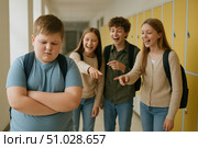 Emotional Contrast in a School Hallway: A Group of Friends Laughing and Pointing at a Peer Who Feels Isolated and Upset, Reflecting the Challenges of Younger Adolescence. Стоковое AI-изображение, AI-художник Башкирова Анна / Фотобанк Лори