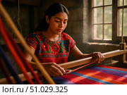 Mexican Artisan Weaving Colorful Textile on Loom. Young Mexican woman in a red floral embroidered blouse weaving vibrant striped fabric on a traditional wooden loom in a rustic workshop. Стоковое AI-изображение, AI-художник Башкирова Анна / Фотобанк Лори