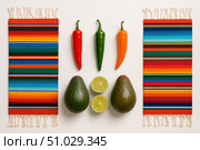 Fresh avocados, chili peppers, and lime arranged between two vibrant striped Mexican table runners on a white background. Стоковое AI-изображение, AI-художник Башкирова Анна / Фотобанк Лори