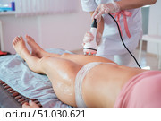 Woman receives an electric massage against cellulite. The doctor performs ultrasonic cavitation correction of the body contours for the patient. Anti-cellulite procedure on the hips in the spa. Стоковое фото, фотограф Михаил Решетников / Фотобанк Лори