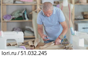 Elderly male tailor cutting out pattern from paper with scissors in sewing workshop. Стоковое видео, видеограф Яков Филимонов / Фотобанк Лори