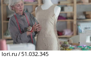 Skillful old tailoress trying prepared dress on mannequin in tailor shop. Стоковое видео, видеограф Яков Филимонов / Фотобанк Лори