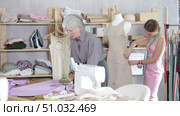 Attentive mature tailoress cutting textile using scissors while other working with mannequin in background. Стоковое видео, видеограф Яков Филимонов / Фотобанк Лори