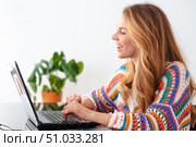 Smiling woman working on laptop at home wearing colorful sweater. Стоковое фото, фотограф Raquel Corcoles Mendez / Фотобанк Лори