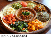 A traditional Ethiopian injera served on a large sourdough flatbread, accompanied by hearty lentil stews, flavorful spiced vegetables, tender doro wat chicken,  created by ai. Стоковое AI-изображение, AI-художник Виталий Сова / Фотобанк Лори