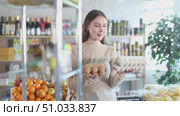 Thoughtful smiling young woman in cozy grocery store holding two different egg cartons, comparing options before deciding to buy. Стоковое видео, видеограф Яков Филимонов / Фотобанк Лори