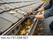 Close up of hand clearing fallen leaves from clogged gutter at home. Стоковое AI-изображение, AI-художник Коханова Наталья / Фотобанк Лори