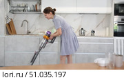 Young woman in homemade blue dress doing household chores. Experienced housewife with vacuum cleaner furbish cleanse carpeting synthetic covering near dining table in kitchen. Стоковое видео, видеограф Яков Филимонов / Фотобанк Лори