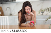 Pleased young woman leaning on table and watching something interesting on her mobile phone in the kitchen. Стоковое видео, видеограф Яков Филимонов / Фотобанк Лори