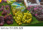 Multi-colored bunches of grapes on a market counter. Juicy yellow and dark red berries are laid out on a green background, next to them are packaged grapes and cherries in transparent containers. The bright and fresh composition emphasizes the richness of choice and the attractiveness of fresh fruits. Стоковое фото, фотограф Анна Кривицкая / Фотобанк Лори
