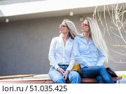 Two surprisingly similar women are sitting on a bench in an embrace and smiling. A middle-aged woman and her elderly mother. Beautiful well-groomed mother and daughter family look. Стоковое фото, фотограф Михаил Решетников / Фотобанк Лори