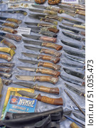 A display case with hunting and fishing knives laid out on a table. The blades are made of different types of steel, some are decorated with engravings. The handles are made of wood, bone and other materials, some of them are wrapped in protective film. The knives vary in shape and size, and are designed for different types of outdoor activities and tourism. Стоковое фото, фотограф Анна Кривицкая / Фотобанк Лори