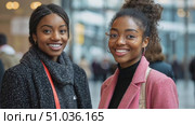 Two women share joyful smiles while interacting at a bustling social gathering, surrounded by an energetic crowd in a lively urban space. Стоковое AI-видео, аниматор Данила Большаков / Фотобанк Лори