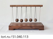 Newton's cradle balancing balls on wooden base demonstrating momentum and energy transfer. Стоковое AI-изображение, AI-художник Иван Рябоконь / Фотобанк Лори