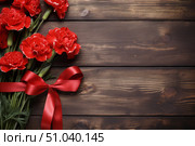 Bouquet of red carnations tied with ribbon lying on rustic wooden table. Стоковое AI-изображение, AI-художник Иван Рябоконь / Фотобанк Лори