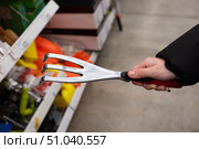 Hand holding a three-pronged garden cultivator tool in a retail store aisles showcasing gardening supplies. Стоковое фото, фотограф Вербицкая Светлана / Фотобанк Лори