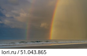 Beautiful double rainbow over the ocean. Two bright multicolored arcs against a blue sky and clouds. Turquoise waves are foaming on a sandy beach. Evening light. Malaysia. Borneo. Kota Kinabalu. Стоковое фото, фотограф Вера Ивановна Кубарева / Фотобанк Лори