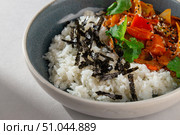 Traditional Korean rice bowl with kimchi-based stew, vegetables, sesame seeds, cilantro and shredded seaweed served in a ceramic bowl on white background. Стоковое фото, фотограф Aleksandr Gavrilychev / Фотобанк Лори