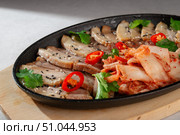 Sliced pork belly served on cast iron plate with traditional Korean kimchi, fresh cilantro, black sesame seeds and red chili peppers for garnish. Стоковое фото, фотограф Aleksandr Gavrilychev / Фотобанк Лори