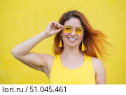 Portrait of a happy woman in sunglasses on a yellow background. Red-haired carefree girl in a dress and earrings tassels of the same color. Lady with an impeccable dazzling smile. Summer photo. Стоковое фото, фотограф Михаил Решетников / Фотобанк Лори