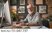 An elderly man with glasses sketches designs and reviews work on his large monitor in a cozy, art-filled home office. Стоковое AI-видео, аниматор Данила Большаков / Фотобанк Лори