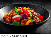 Sweet sour pork with colorful peppers, mixed vegetables served in a black bowl on dark concrete background. Traditional Chinese dish. Close-up. The meat pieces in a brown sauce glaze. Sichuan cuisine. Стоковое AI-изображение, AI-художник Марина Демидюк / Фотобанк Лори