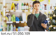 Man talks on phone while shopping in household store and consults with wife about purchase. Client walks around store and chats on phone, answers call. Стоковое видео, видеограф Яков Филимонов / Фотобанк Лори
