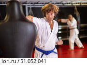 Blue‑belt karateka punching training dummy in gym. Стоковое фото, фотограф Яков Филимонов / Фотобанк Лори