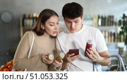 Young girl with husband in big supermarket scan QR code bottle of smoothie. Couple of buyers friends take photo information on packaging of bio product. Стоковое видео, видеограф Яков Филимонов / Фотобанк Лори