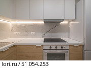 Modern kitchen with white cabinets, marble backsplash, and stainless steel appliances. Clean and minimalist design with bright lighting. Стоковое фото, фотограф PAv / Фотобанк Лори